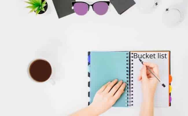 a photo of a hand with a pen over a notebook with the word Bucket List