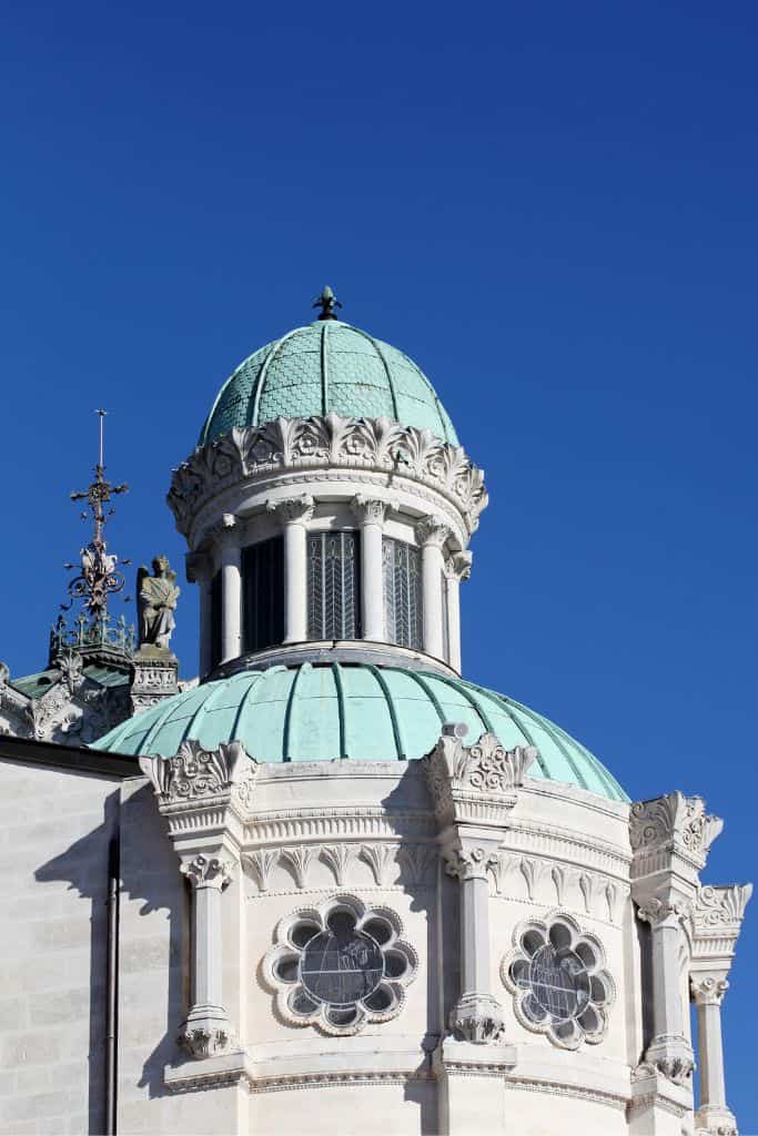 Close-up of the Sanctuary of St. John Vianney in Ars, one of the notable Catholic pilgrimage sites in France, featuring its elegant green domes, rose windows, and ornate stone detailing under a clear blue sky. The architecture reflects the site's deep spiritual and historical significance.