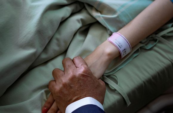 photo of a hand holding a hand of someone sick in a hospital bed to signify visiting someone sick as one of the Catholic staycation ideas